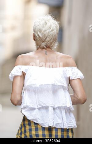Une femme portant une chemise blanche et une jupe à carreaux jaune et bleu descend une rue. Concept de désinvolture et de simplicité, comme la femme est habillée en co Banque D'Images