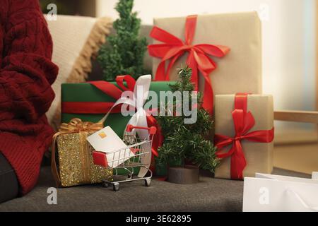 Gros plan d'un panier avec une carte de crédit à côté de cadeaux de Noël magnifiquement emballés. Ambiance shopping des fêtes Banque D'Images