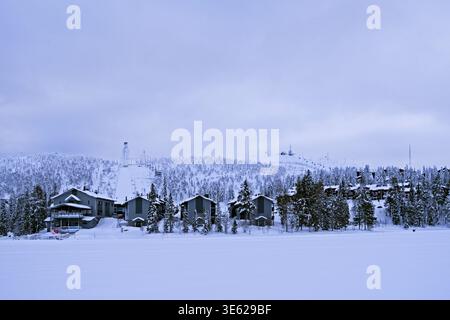 Kuusamo, Finlande – 11.02.2019 : vue sur le lac Talvijaervi gelé jusqu’au domaine skiable de Ruka avec le saut à ski et les remontées mécaniques autour de la chute de Rukatunturi Banque D'Images