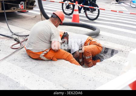 Deux ouvriers industriels en équipement de sécurité orange sur un chantier de construction avec des barrières de travaux routiers et de l'équipement Banque D'Images