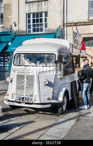 Une camionnette Citroën H blanche vintage convertie en camion de restauration de rue garée sur une place publique pendant qu'un client attend près de la fenêtre de service Banque D'Images