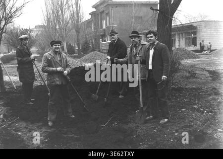 Slavyansk, 17 avril 1982, armature-isolateur usine. Une équipe de cinq ouvriers d'usine posent solennellement avec des pelles tout en se tenant autour d'un grand tas de terre sombre pendant le subbotnik communiste. Les hommes sont regroupés à l'extérieur dans la zone verte près du bâtiment de l'entreprise un jour de printemps. Une authentique photographie d'archives historiques véhiculant l'esprit confiant du travail bénévole collectif, la vie quotidienne industrielle soviétique authentique, la camaraderie professionnelle sur le lieu de travail et le Donbass paisible. Banque D'Images