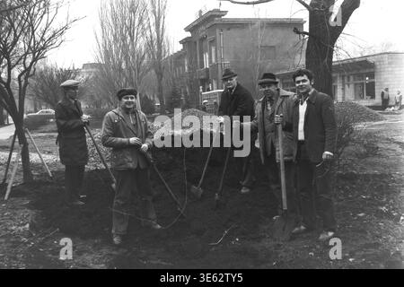 Slavyansk, 17 avril 1982, armature-isolateur usine. Une équipe de cinq ouvriers d'usine posent solennellement avec des pelles tout en se tenant autour d'un grand tas de terre sombre pendant le subbotnik communiste. Les hommes sont regroupés à l'extérieur dans la zone verte près du bâtiment de l'entreprise un jour de printemps. Une authentique photographie d'archives historiques véhiculant l'esprit confiant du travail bénévole collectif, la vie quotidienne industrielle soviétique authentique, la camaraderie professionnelle sur le lieu de travail et le Donbass paisible. Banque D'Images