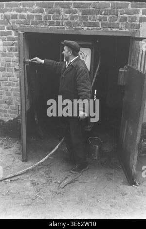 Slavyansk, 17 avril 1982, armature-isolateur usine. Un ouvrier masculin concentré dans une casquette et une veste utilise un petit pinceau pour peindre soigneusement le cadre de porte métallique d'un bâtiment industriel en brique pendant le subbotnik communiste de masse. Il est engagé dans la réparation cosmétique saisonnière et l'entretien du territoire de l'entreprise un jour de printemps. Une authentique photographie d'archives historiques transmettant l'esprit du travail bénévole personnel dévoué, la vie quotidienne de fabrication soviétique authentique et l'atmosphère du Donbass paisible. Banque D'Images