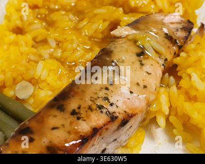 Gros plan macro d'un filet de poisson grillé servi sur du riz jaune vif avec des haricots verts visibles sur le côté. Le poisson semble être du saumon ou Banque D'Images