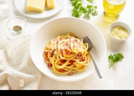 Plat de pâtes italiennes avec pancetta croustillante, fromage parmesan et poivre noir dans un bol en céramique blanche sur fond clair. Vue rapprochée Banque D'Images
