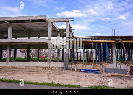 Ossature en béton de chantier abandonné sous ciel bleu. L'échafaudage et les poutres en bois restent inactifs. Terre sale avec de l'herbe clairsemée et dispersée Banque D'Images