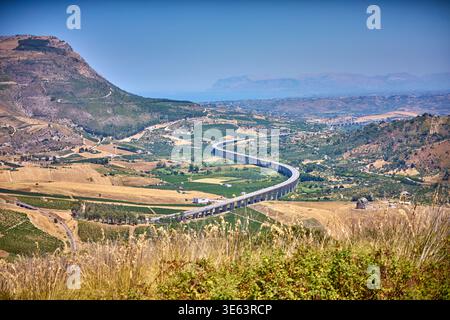 Une vue panoramique sur un viaduc autoroutier surélevé sinueux traversant une vallée agricole luxuriante en Italie. L'autoroute en béton serpente à travers le patchwork Banque D'Images
