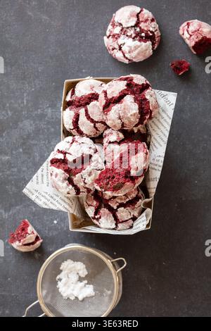 Délicieux biscuits froissés de velours rouge saupoudrés de sucre en poudre, présentés dans un cadre rustique. Banque D'Images