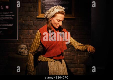 Une figure de cire réaliste d'une femme vêtue de vêtements de la classe ouvrière du XVIIIe ou XIXe siècle se tient dans une exposition de musée faiblement éclairée avec des murs de briques. Banque D'Images