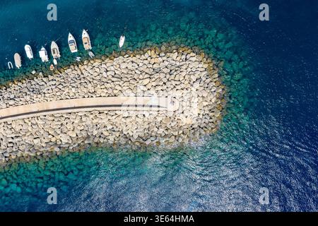 Vue aérienne du brise-lames rocheux et de l'entrée du port près de Mgarr, Gozo, avec de petits bateaux amarrés à côté de la jetée de pierre dans la mer bleue claire. Banque D'Images