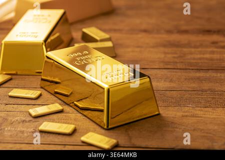 Image de haute qualité de lingots d'or brillants et de lingots de métaux précieux plus petits affichés sur une table en bois riche avec un éclairage naturel chaud, parfait pour Banque D'Images