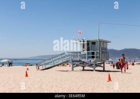 Tour de sauveteur avec un drapeau américain sur la plage de sable de Santa Monica, Californie, sous un ciel bleu clair avec des montagnes en arrière-plan. Banque D'Images