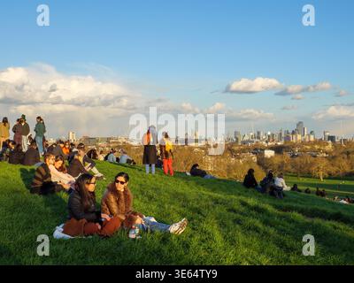 Des jeunes assis sur l'herbe et regardant l'horizon de la ville au sommet du parc Primrose Hill, Londres, Royaume-Uni Banque D'Images