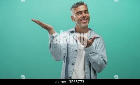 Homme d'âge moyen avec les cheveux gris portant une chemise légère, montrant les paumes ouvertes et présentant une paume jusqu'à la caméra dans un studio turquoise toile de fond ; sympathique i Banque D'Images