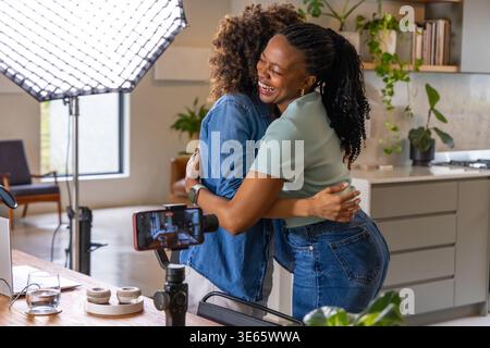 Deux femmes afro-américaines serrées dans la cuisine avec trépied smartphone, softbox et ordinateur portable Banque D'Images