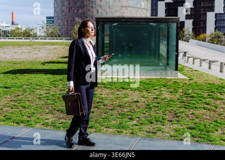 Femme d'affaires marchant dans le parc de la ville avec smartphone Banque D'Images