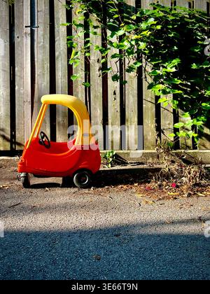 Une petite voiture rouge et jaune abandonnée se trouve près d'une clôture en bois Banque D'Images