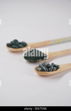 Suppléments de spiruline et poudre dans des cuillères en bois Superfood vert sain sur fond blanc Banque D'Images