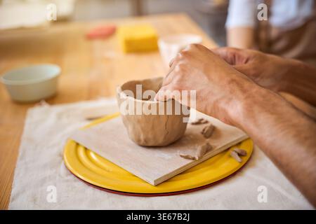 Femme adulte concentrée sur la création d'un pot en céramique à l'aide d'une roue de poterie dans un studio intérieur lumineux. Des outils d'artisanat l'entourent alors qu'elle exprime sa créativité Banque D'Images