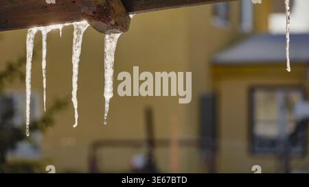 Glaçons fondant et dégouttant l'eau d'une poutre en bois pendant une froide journée d'hiver Banque D'Images