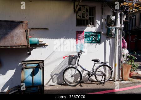 Taipei, Taïwan - 18 novembre 2023 : un vélo s'appuie contre un mur d'allée ensoleillé marqué d'un Zhongshan N. Rd. vert panneau de rue et avis affichés. Banque D'Images