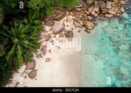 Le sable baigné de soleil et les eaux turquoises créent une toile de fond époustouflante tandis que les voyageurs se détendent sur la plage sereine de Baie Sainte Anne. Une végétation luxuriante encadre ce paradis tropical. Couple à Anse Volbert Praslin Banque D'Images