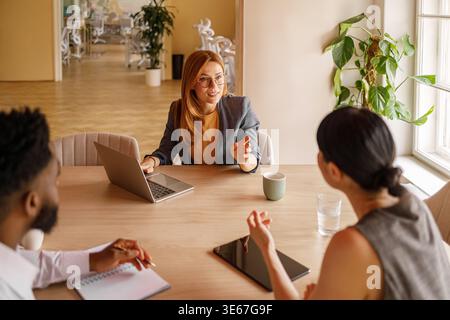 Vue en angle élevé de la femme d'affaires expliquant les stratégies à des collègues tout en collaborant sur ordinateur portable pendant la réunion de bureau Banque D'Images