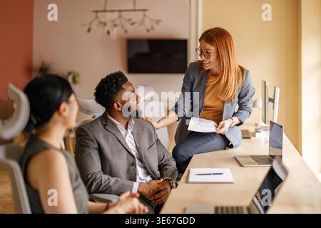 Collègues professionnels heureux partageant des idées avec des documents et des ordinateurs portables lors d'une réunion stratégique dans un bureau moderne Banque D'Images