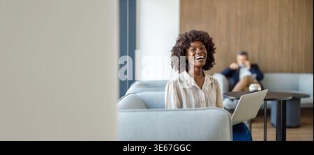 Portrait de femme d'affaires heureuse riant tout en travaillant sur un ordinateur portable sur un canapé confortable dans un bureau moderne Banque D'Images