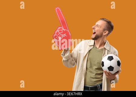 Ventilateur de football masculin avec balle et main de mousse sur fond orange Banque D'Images