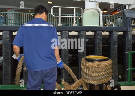 Débardeur sur le pont du ferry manipulant des cordes d'amarrage épaisses dans un terminal portuaire Star à Hong Kong, Chine, le 23 juillet 2015 Banque D'Images