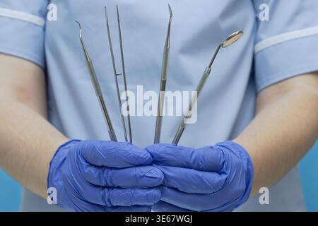 Gros plan d'un dentiste professionnel ou d'un assistant dentaire portant des gants bleus en nitrile et un uniforme médical, tenant un ensemble de diag dentaire en acier inoxydable Banque D'Images