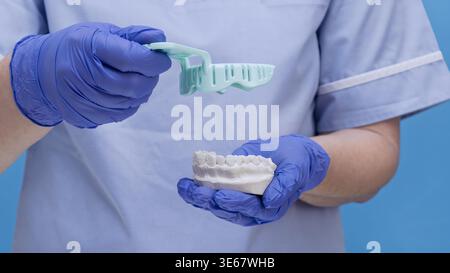 Gros plan des mains d'un dentiste ou d'un technicien dentaire en gants bleus en nitrile. Le médecin tient un porte-empreinte dentaire en plastique et un pla blanc Banque D'Images