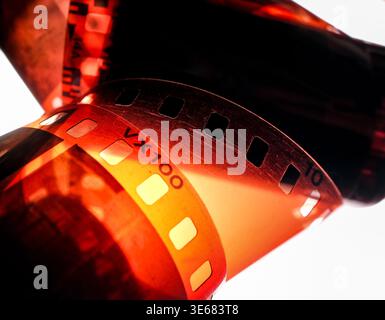 Gros plan d'une bande de film photographique orange de 35 mm avec des trous pour pignons et un code imprimé VX100, tons chauds contre-éclairés Banque D'Images
