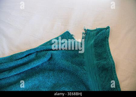 Une serviette de salle de bain vert foncé et ancienne avec un coin déchiré sur un fond de matériau blanc et un espace de copie Banque D'Images