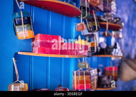 Savons faits à la main de différentes couleurs et formes sont soigneusement disposés sur des étagères en bois contre un mur bleu vif dans un environnement de marché Banque D'Images
