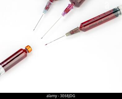 Plusieurs seringues médicales remplies de liquide sanguin rouge profond sont disposées avec un flacon en verre sur fond blanc. La plus grande seringue est clairement étiquetée Banque D'Images