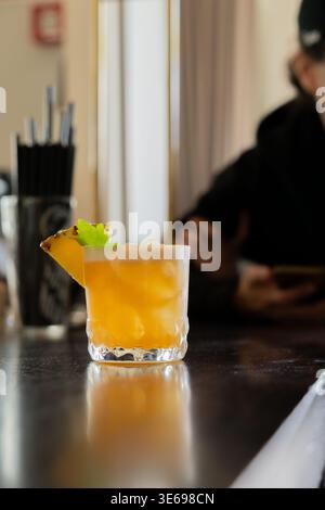 Un verre rempli d'une boisson de couleur orange se trouve sur un comptoir de bar. Il est garni d'une tranche d'ananas et d'un brin de menthe. Les glaçons sont visibles, Banque D'Images