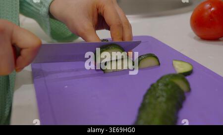 Gros plan des mains coupant le concombre sur une planche violette Banque D'Images