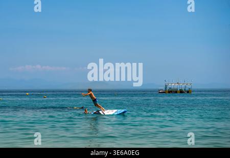 Un jeune homme sautant dans la mer depuis un paddleboard à la plage de Barbati. Loisirs estivaux et activités aquatiques sur l'île de Corfou, Grèce, 12 juillet 2023. Banque D'Images