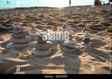 Pierres zen empilées sur une plage de sable fin pendant l'heure dorée. Concept d'équilibre, d'harmonie et de tranquillité estivale sur la côte de Corfou, Grèce. Banque D'Images