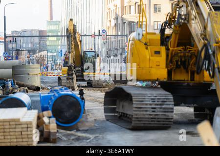 Chantier de construction urbain actif avec plusieurs pelles sur chenilles jaunes et de grandes conduites bleues pour réseau municipal d'eau ou de gaz infrastruc Banque D'Images