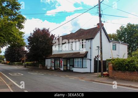 Bâtiment blanc traditionnel avec des drapeaux Union Jack sur les fenêtres, un toit en tuiles et un panneau de limitation de vitesse, capturant une scène de village anglais classique. Banque D'Images