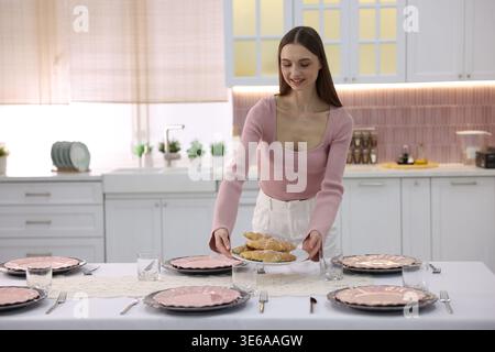 Cadre magnifique. Femme souriante mettant une assiette avec des croissants sur la table dans la cuisine Banque D'Images