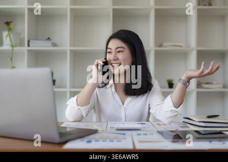 Jeune femme d'affaires asiatique souriant et parlant sur téléphone portable au bureau Banque D'Images