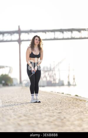 Femme active debout sur un chemin de front de mer, tenant une corde à sauter avant l'exercice Banque D'Images
