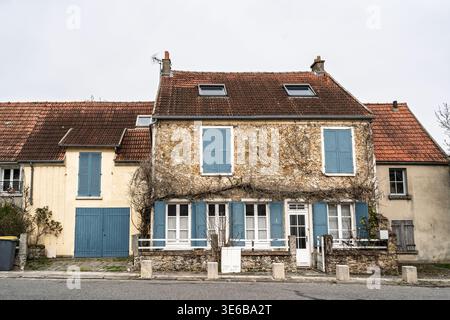 Vue de face d'une ancienne maison d'habitation française dans un village, montrant des murs de pierre, des volets bleus et un toit carrelé, illustrant un logement traditionnel, rural Banque D'Images