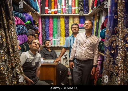 ISPAHAN, IRAN - 20 AOÛT 2016 : quatre vendeurs de tissus posent à l'intérieur d'un petit magasin de textile dans le bazar d'Ispahan, iran, entouré de rouleaux colorés de tissu A. Banque D'Images