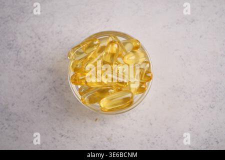 capsule d'huile de poisson disposée dans un bol en verre transparent sur une surface légère Banque D'Images